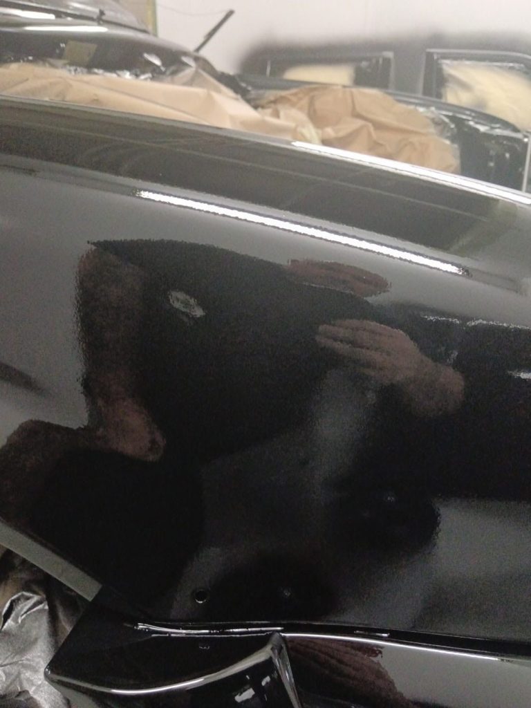 Close-up of black paintwork with a mirror finish reflecting the workshop
