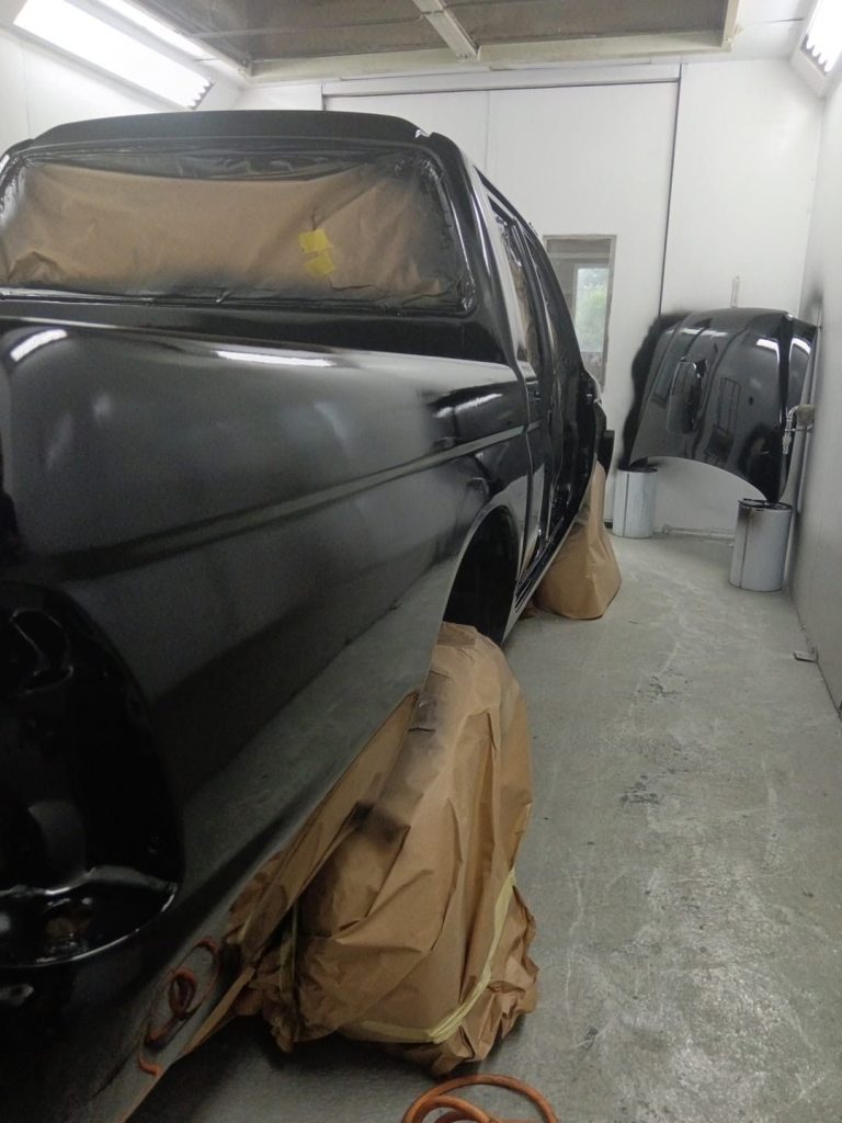 Black pickup masked up in the spray booth, bonnet on a stand alongside
